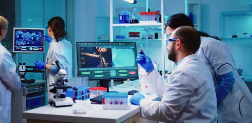 Microbiologist doctor taking a blood sample tube from rack with machines of analysis in the lab background. Doctors examining vaccine evolution using high tech researching diagnosis against covid19